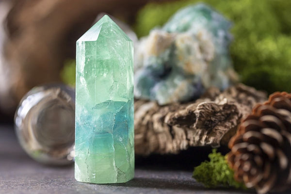 teal gemstone tower against greenery and pine cones